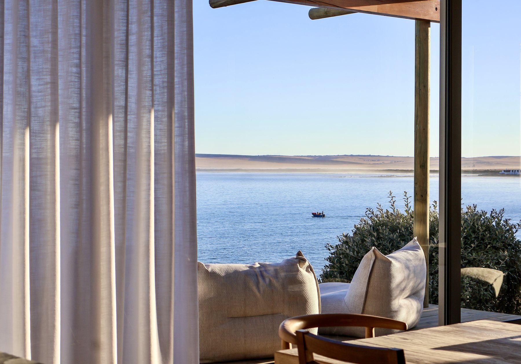 A beach house lounge open to the bay, a fishing boat crossing the water